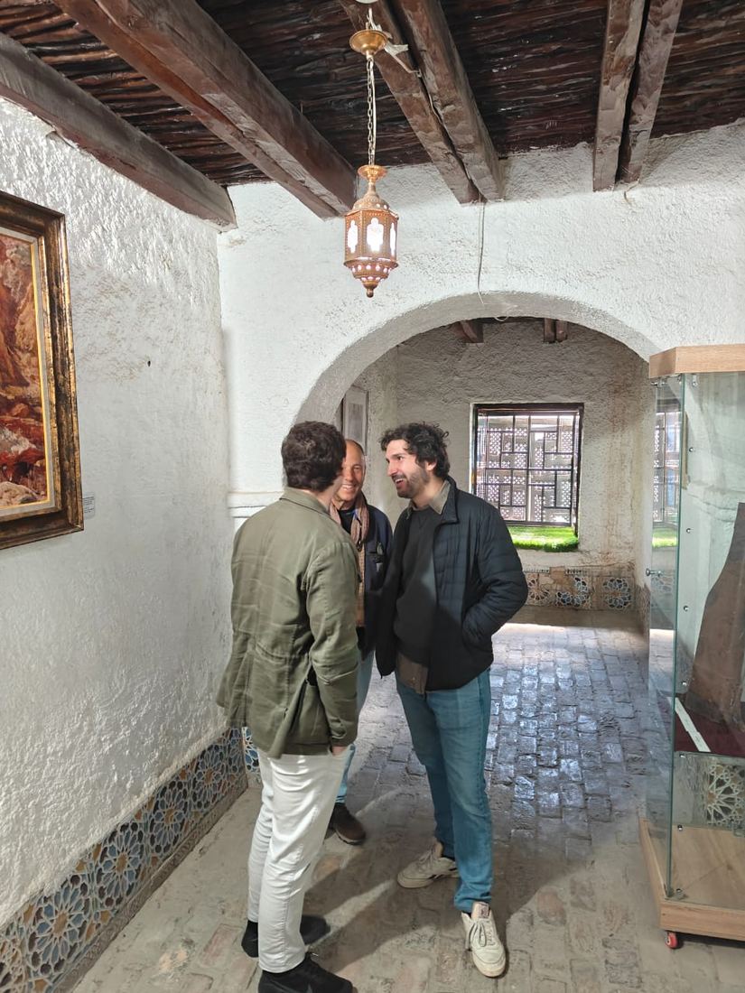 Tre viaggiatori chiacchierano sotto l'arco a volta imbiancato di una casa storica, con una lanterna traforata sopra di loro
