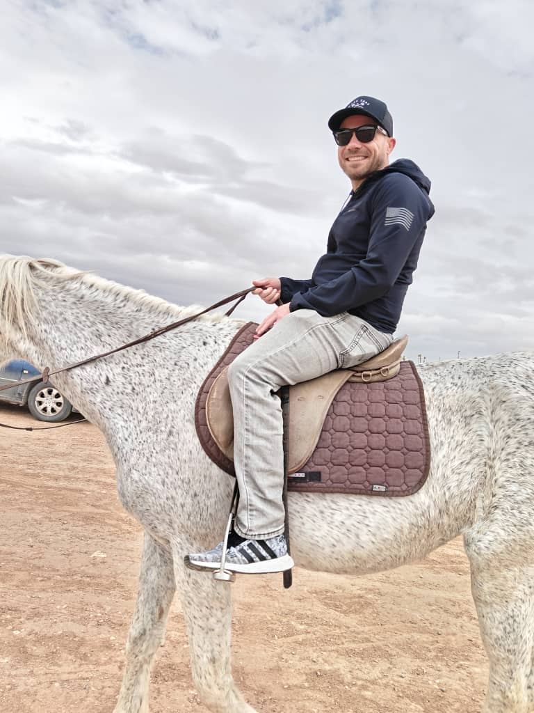 Un viaggiatore in sella a un cavallo grigio su una pista sabbiosa