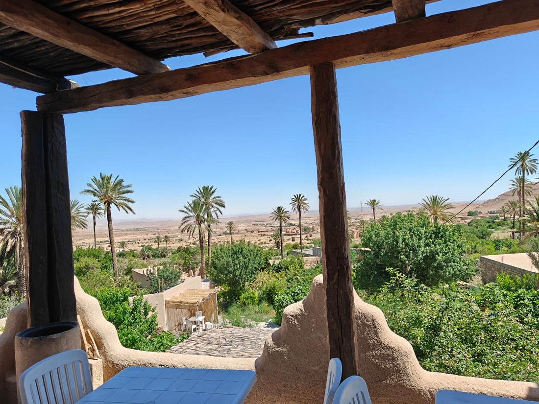 La vista da una terrazza ombreggiata da travi di palma spaccate, su un'oasi di palme e sul deserto oltre