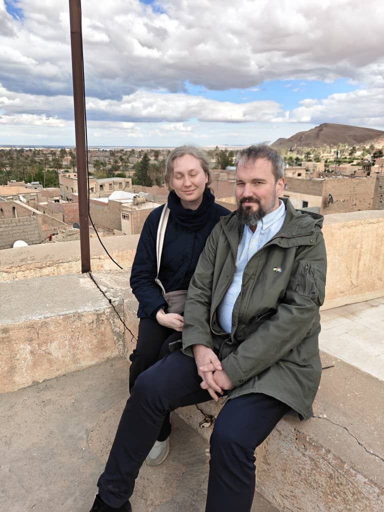 Una coppia seduta su un tetto sopra una città del deserto dai tetti piatti