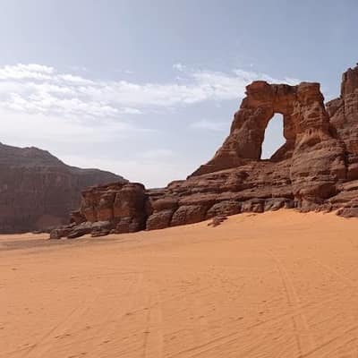 A natural sandstone arch above orange sand in the desert around Djanet