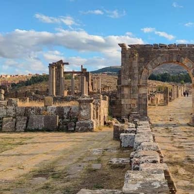 A paved Roman street lined with columns leading to the Arch of Caracalla at Djémila
