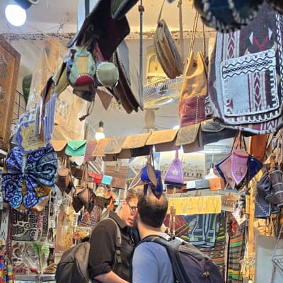 Travellers browsing a M'Zab craft shop hung with leather bags, basketry and woven textiles