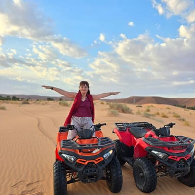 A traveller standing arms outstretched between two quad bikes on the sand at the end of the afternoon