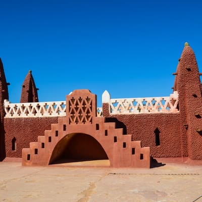 The red Sudanese-style gate of Timimoun, its pointed towers against a blue sky
