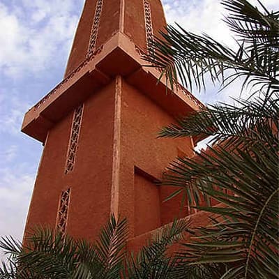 A red earthen minaret rising behind palms in Timimoun