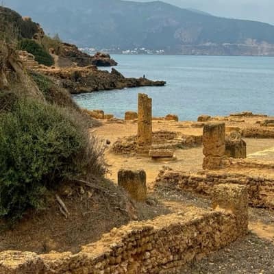 A lone column above the rocky shore at Tipaza, with mountains across the bay