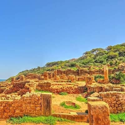 Low Roman walls on a grassy slope above the sea at Tipaza