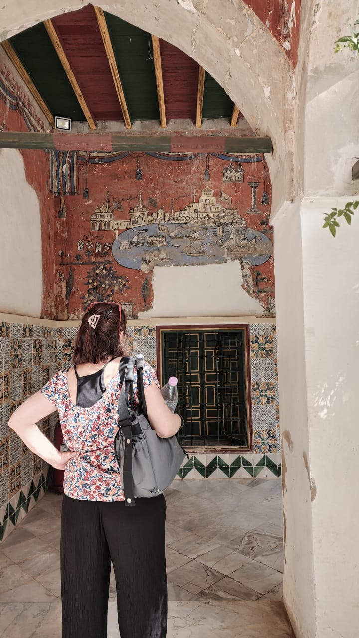 A naive wall painting of a harbour city above zellige tiling inside the Ahmed Bey Palace, Constantine