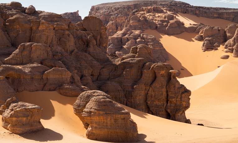 Eroded sandstone outcrops and a long dune slope in the red Tadrart