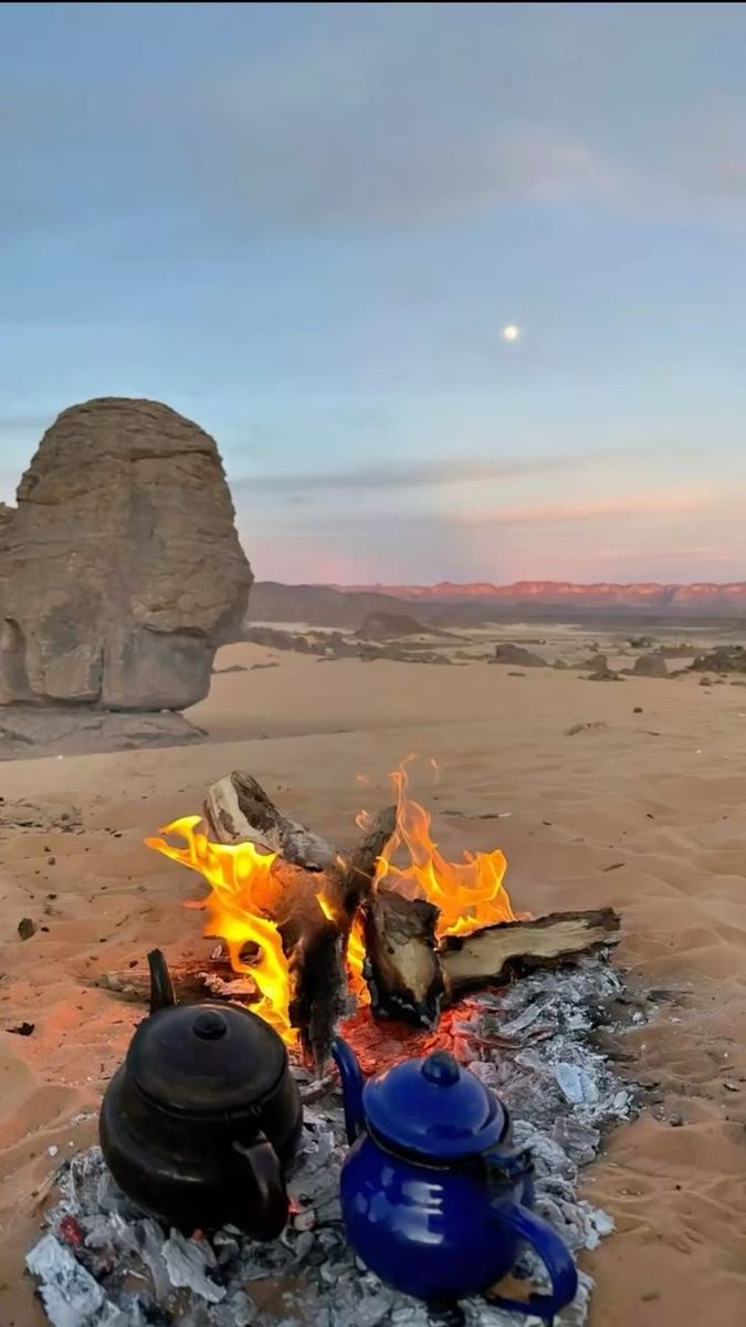 A campfire burning on the sand beside a great boulder at a desert camp near Djanet