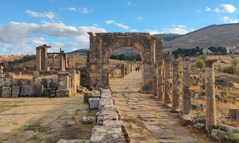 A paved Roman street lined with columns leading to the Arch of Caracalla at Djémila