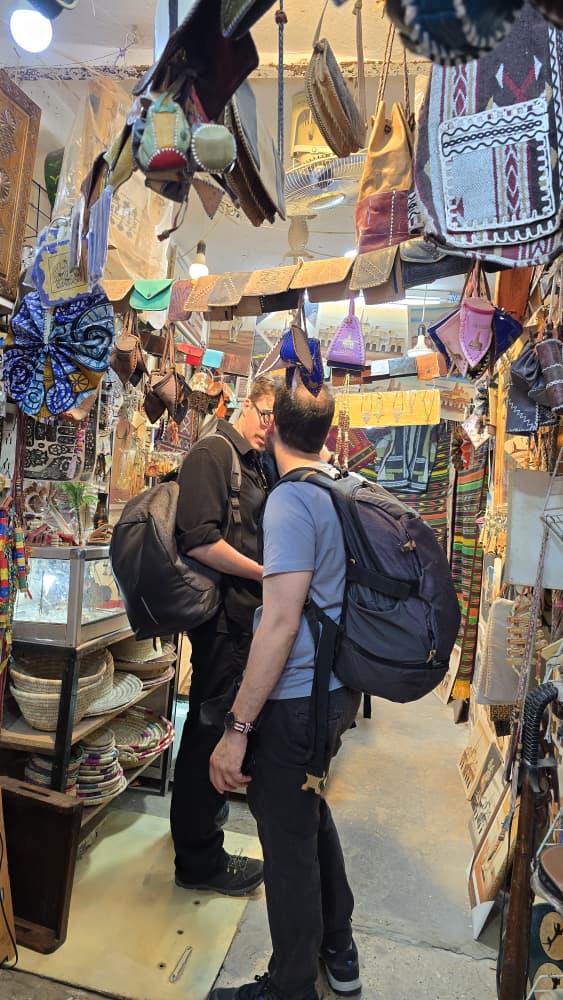 Travellers browsing a M'Zab craft shop hung with leather bags, basketry and woven textiles