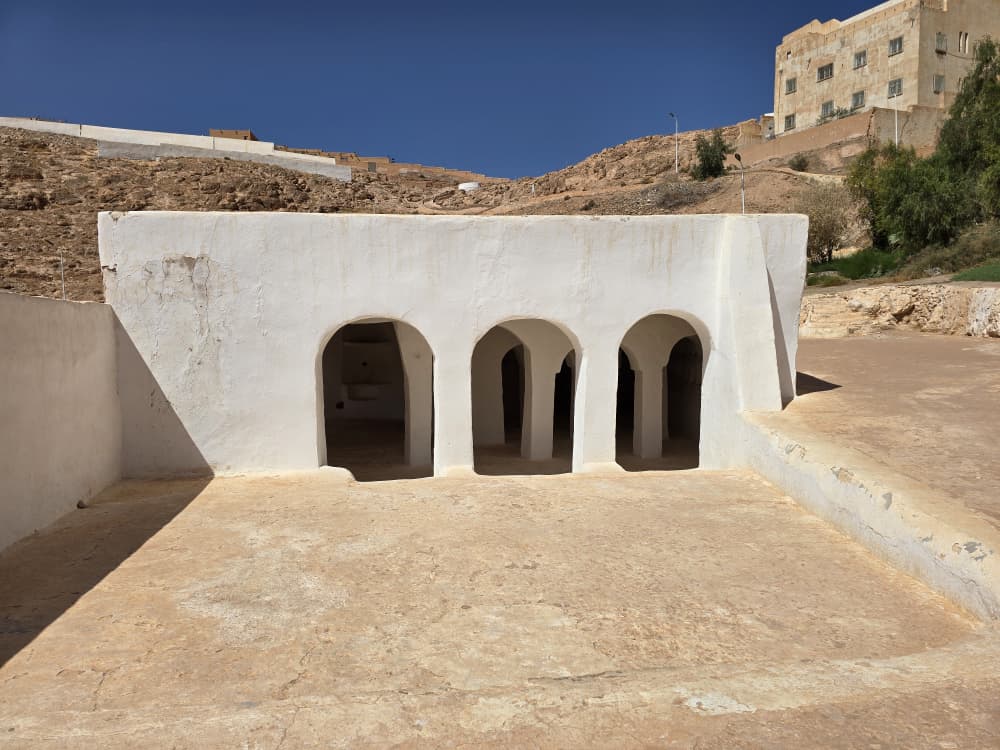 The whitewashed arcaded front of a M'Zab prayer hall, cut into the slope below the town