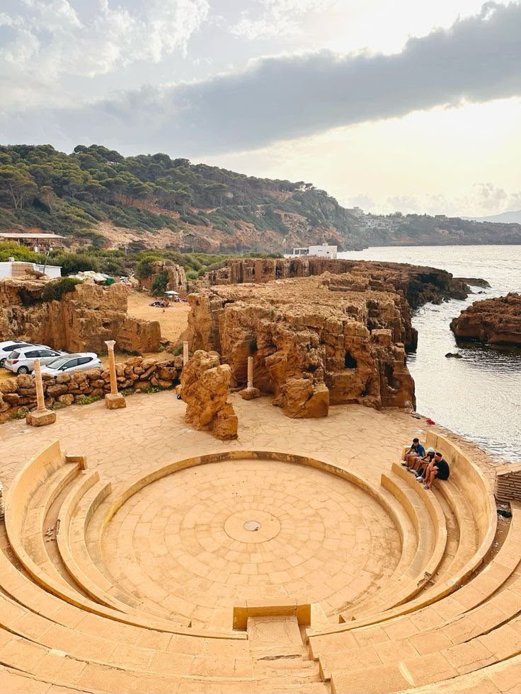 A semicircular Roman structure among ruins at the water's edge in Tipaza
